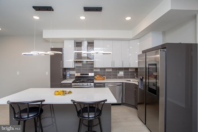 kitchen with a breakfast bar, stainless steel appliances, a sink, wall chimney range hood, and modern cabinets