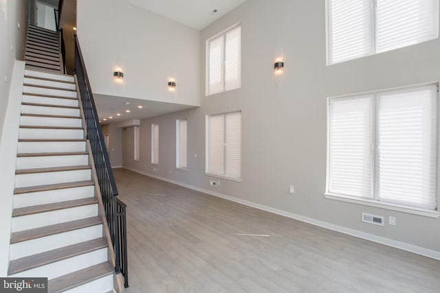 unfurnished living room featuring stairway, a high ceiling, visible vents, and wood finished floors