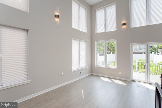 unfurnished living room with wood finished floors, a towering ceiling, and baseboards