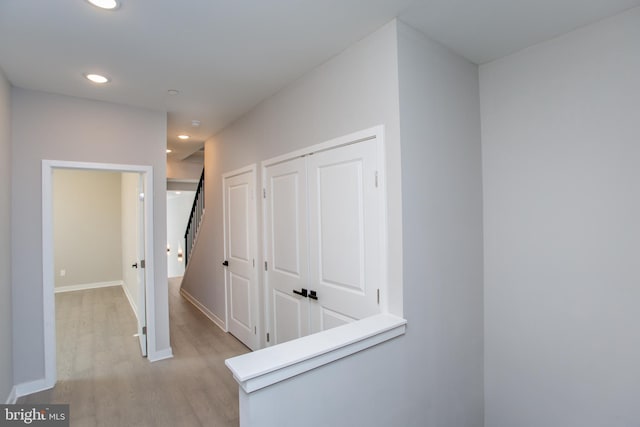 hall featuring baseboards, light wood-type flooring, and recessed lighting