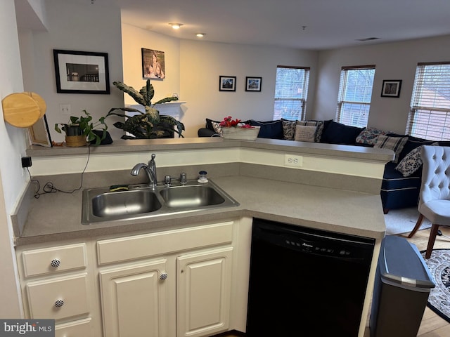 kitchen with black dishwasher, open floor plan, a peninsula, white cabinetry, and a sink