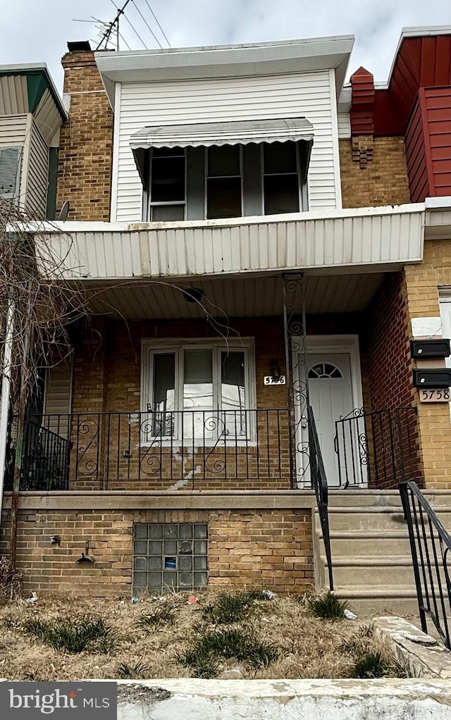 townhome / multi-family property featuring covered porch, brick siding, and a chimney