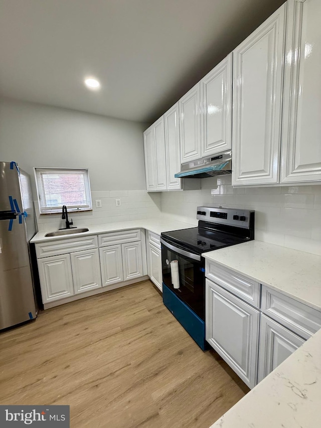 kitchen featuring under cabinet range hood, a sink, white cabinetry, electric stove, and freestanding refrigerator