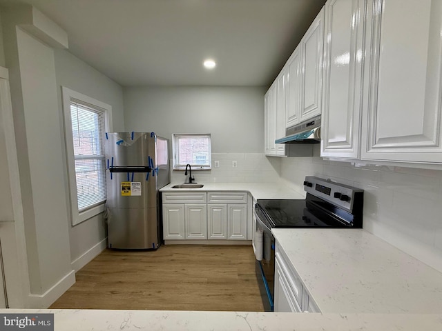 kitchen with light wood finished floors, a sink, stainless steel appliances, under cabinet range hood, and backsplash