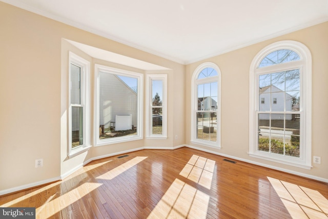 interior space with wood-type flooring, visible vents, baseboards, and ornamental molding