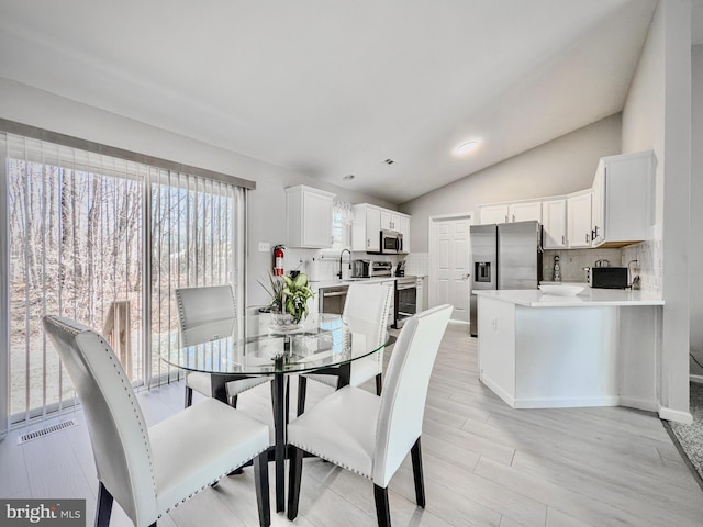 dining area featuring visible vents, vaulted ceiling, and light wood finished floors