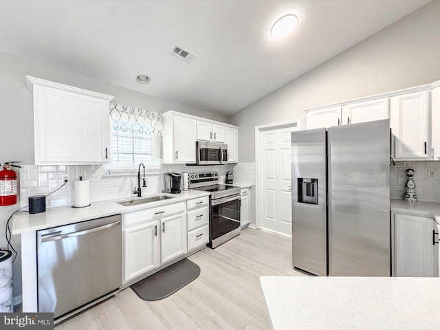 kitchen with visible vents, white cabinets, lofted ceiling, stainless steel appliances, and a sink