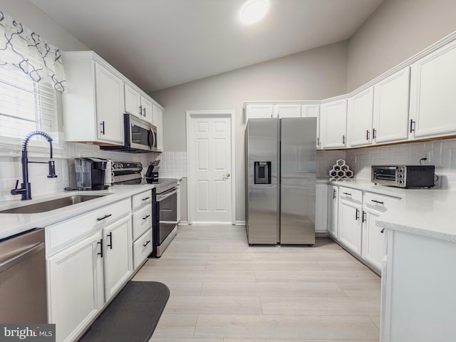 kitchen with a toaster, lofted ceiling, appliances with stainless steel finishes, white cabinets, and a sink