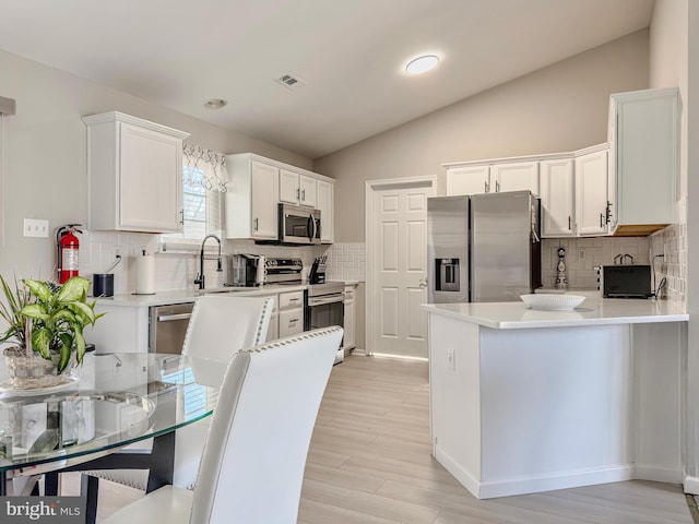 kitchen with visible vents, appliances with stainless steel finishes, a peninsula, vaulted ceiling, and white cabinetry