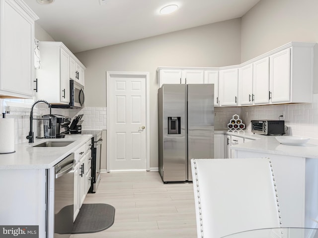 kitchen with tasteful backsplash, lofted ceiling, stainless steel appliances, white cabinetry, and a sink