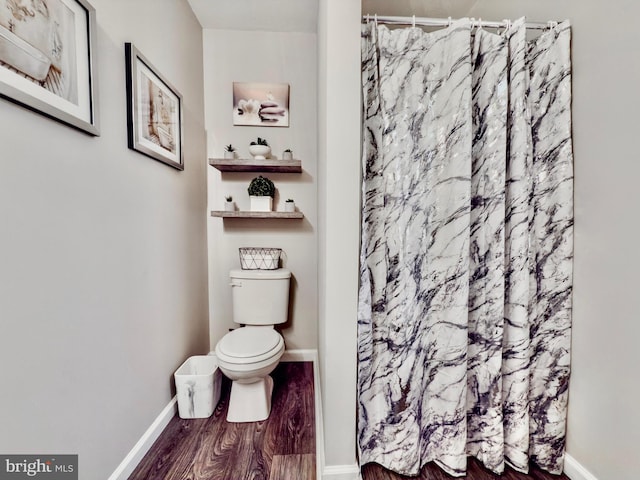 bathroom with toilet, a shower with curtain, baseboards, and wood finished floors