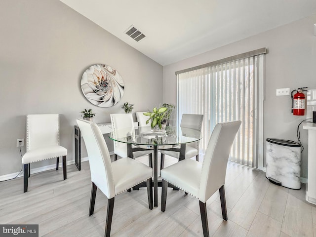 dining room with light wood-style flooring, visible vents, vaulted ceiling, and baseboards