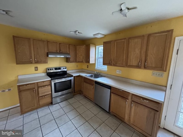 kitchen featuring brown cabinets, stainless steel appliances, light countertops, under cabinet range hood, and a sink