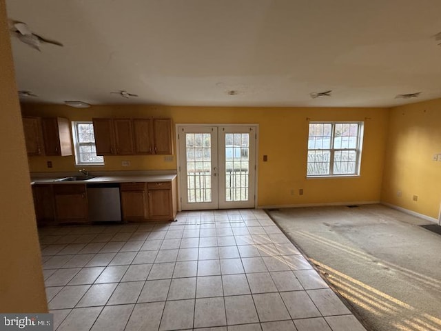 kitchen with light tile patterned floors, brown cabinetry, light colored carpet, stainless steel dishwasher, and a sink