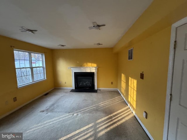 unfurnished living room featuring carpet, a fireplace with flush hearth, visible vents, and baseboards