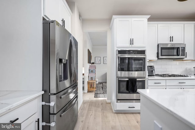 kitchen with light wood-type flooring, decorative backsplash, appliances with stainless steel finishes, and white cabinets