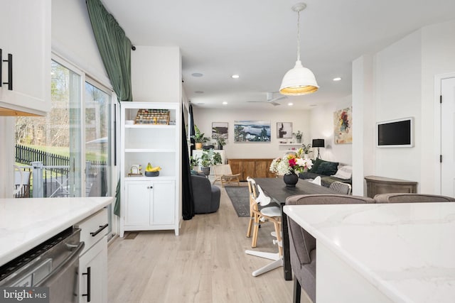 kitchen with light stone countertops, light wood-style flooring, hanging light fixtures, white cabinets, and dishwasher