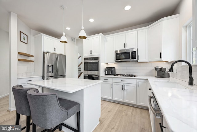 kitchen featuring tasteful backsplash, a kitchen island, appliances with stainless steel finishes, white cabinetry, and a sink