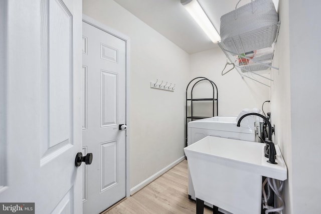 clothes washing area with a sink, washer / clothes dryer, light wood finished floors, baseboards, and laundry area