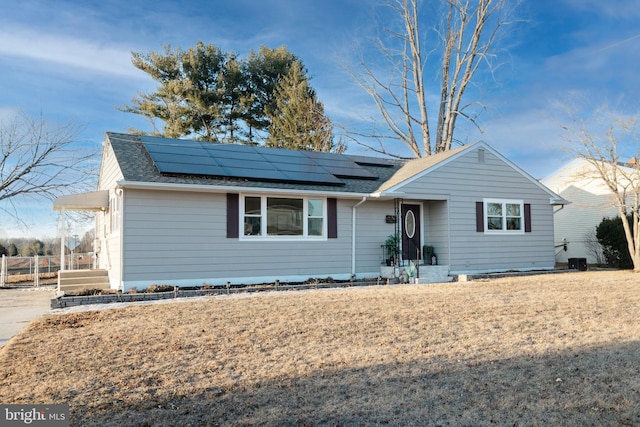 ranch-style house featuring a shingled roof, a front yard, and roof mounted solar panels