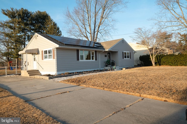 ranch-style home featuring roof mounted solar panels and a front lawn