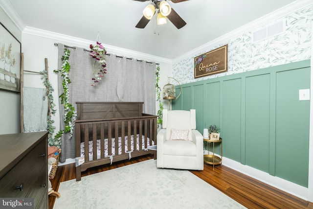 bedroom with a decorative wall, crown molding, wood finished floors, a nursery area, and wallpapered walls