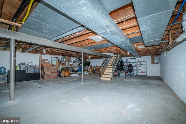 unfinished below grade area featuring concrete block wall, electric panel, and stairway