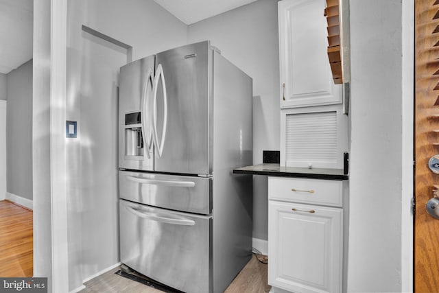 kitchen with white cabinets, dark countertops, light wood-type flooring, and stainless steel refrigerator with ice dispenser