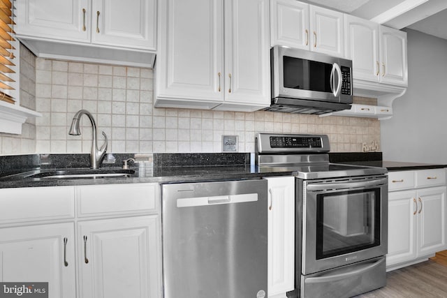 kitchen featuring appliances with stainless steel finishes, white cabinetry, a sink, and tasteful backsplash