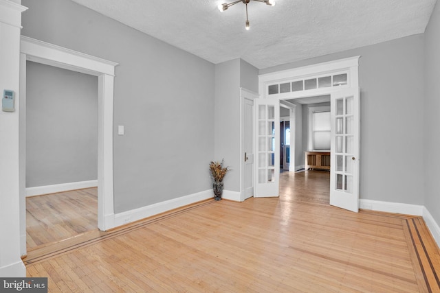 unfurnished room with a textured ceiling, french doors, wood-type flooring, and baseboards