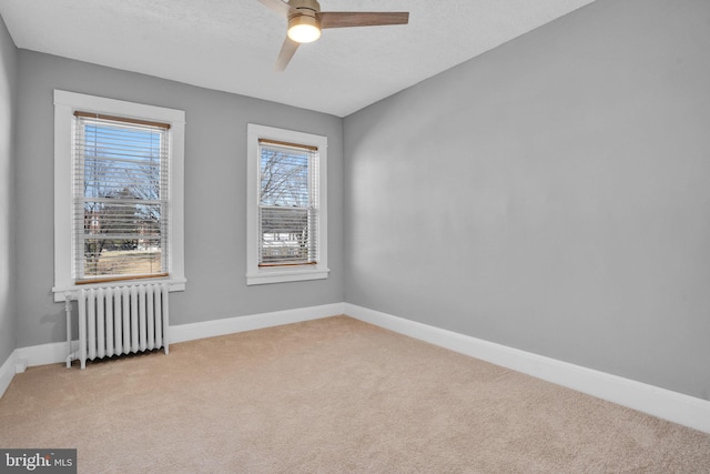 spare room featuring baseboards, ceiling fan, light colored carpet, and radiator