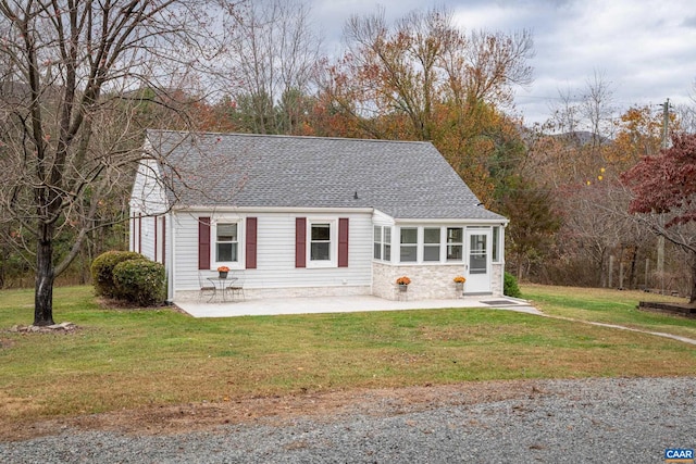 view of front of home featuring stone siding, roof with shingles, a front yard, and a patio