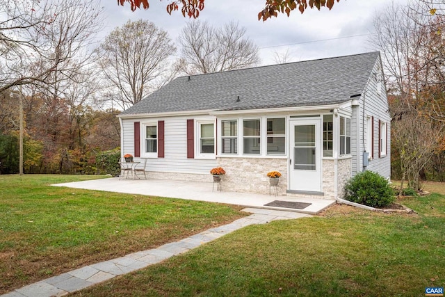 view of front of house with stone siding, a shingled roof, a front lawn, and a patio