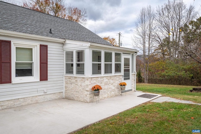 view of side of home with a yard, stone siding, a patio, and roof with shingles