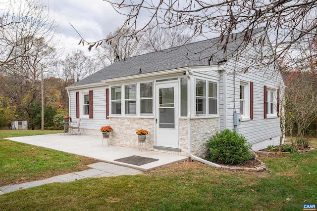 view of front of home with stone siding, roof with shingles, a patio, and a front yard