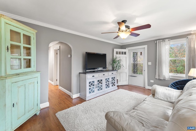 living area with baseboards, crown molding, arched walkways, and wood finished floors