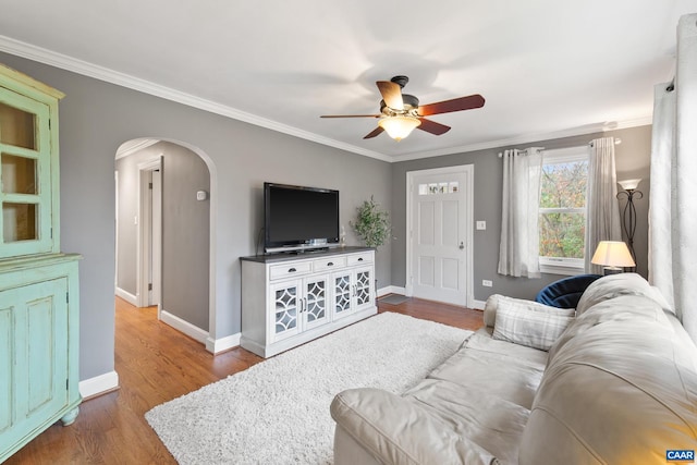 living area featuring baseboards, arched walkways, ceiling fan, wood finished floors, and crown molding