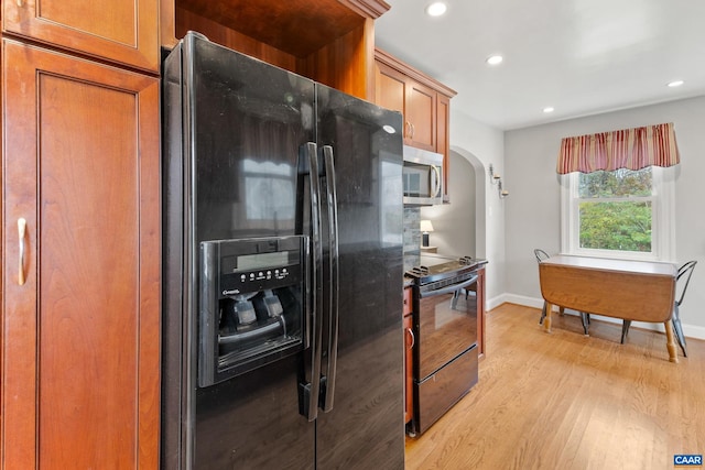 kitchen with arched walkways, black appliances, baseboards, and light wood-style floors