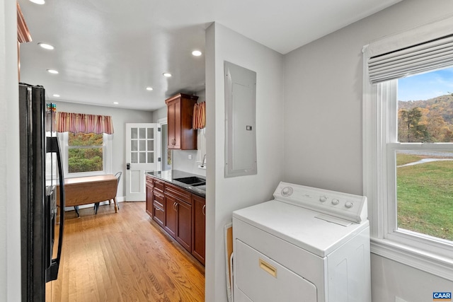 clothes washing area featuring light wood-style flooring, a sink, washer / dryer, laundry area, and electric panel