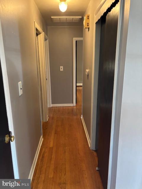 corridor with baseboard heating, wood finished floors, visible vents, and baseboards