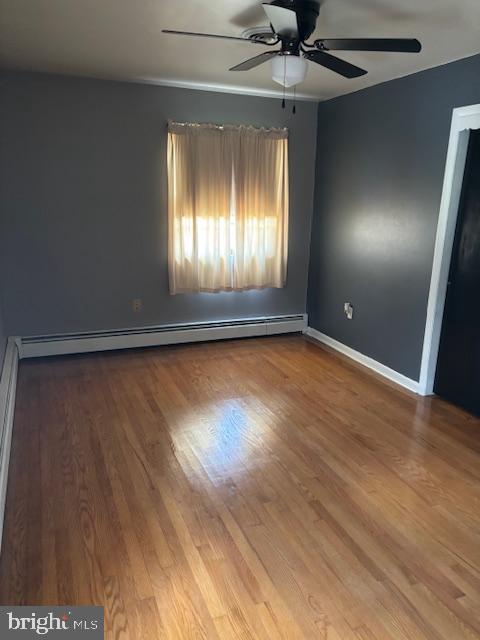 spare room with baseboard heating, wood finished floors, a ceiling fan, and baseboards