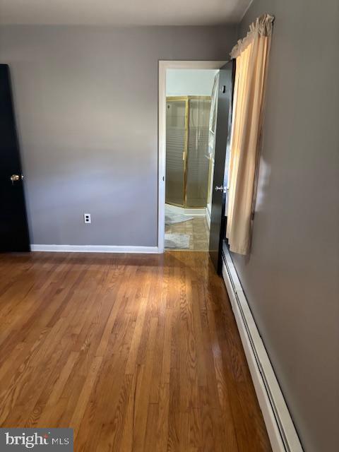 unfurnished bedroom with baseboards, connected bathroom, baseboard heating, and wood finished floors