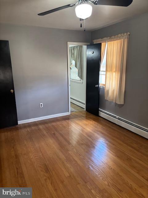 unfurnished room featuring a baseboard radiator, ceiling fan, baseboards, and wood finished floors