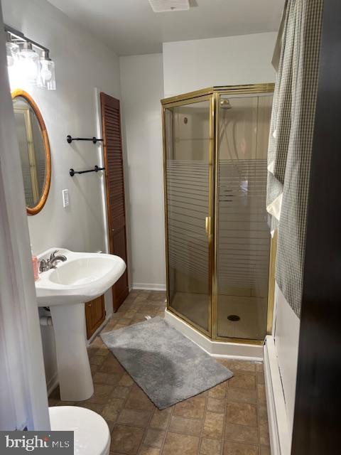 bathroom featuring a sink, toilet, a shower stall, and baseboard heating