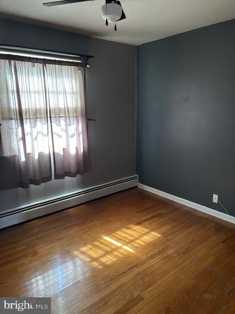 unfurnished room featuring a ceiling fan, a baseboard radiator, baseboards, and wood finished floors