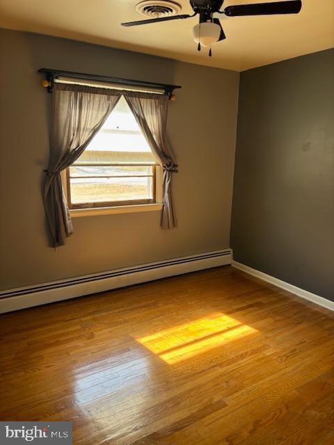 unfurnished room featuring baseboard heating, wood finished floors, a ceiling fan, and baseboards