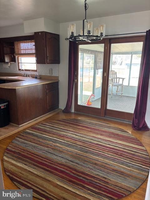 kitchen featuring wood finished floors, an inviting chandelier, light countertops, dark brown cabinets, and pendant lighting