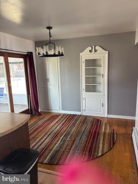 unfurnished dining area with a chandelier, baseboard heating, wood finished floors, and baseboards