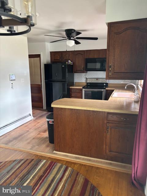 kitchen with light wood-type flooring, baseboard heating, a sink, and black appliances