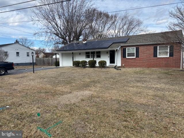 single story home with roof mounted solar panels, brick siding, fence, and a front lawn